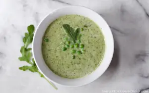 white bowl of green goddess soup with peas and arugula garnish