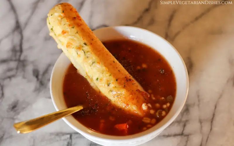 breadstick in bowl of soup with golden spoon