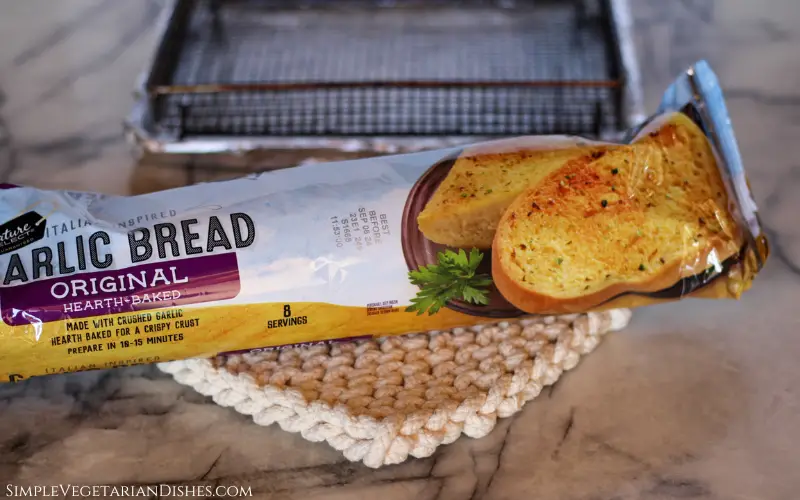 frozen garlic bread in air fryer ingredients on white knit potholder with wire basket in background