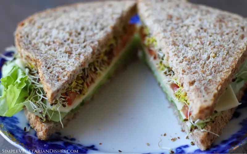 sandwich with cheese, lettuce, tomato, alfalfa sprouts and mustard sliced diagonally on blue china plate