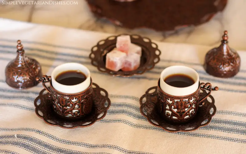 two cups with saucers and sweets in background