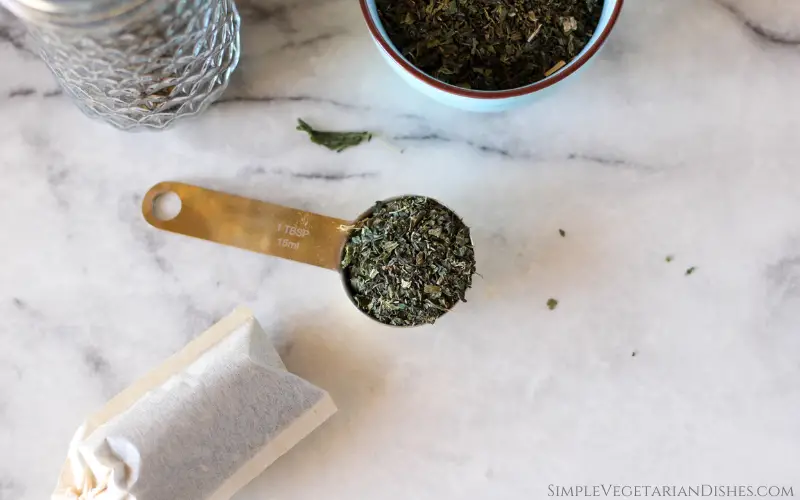 health benefits of nettle tea image dried nettle leaves measured out into golden tablespoon with teabag in foreground