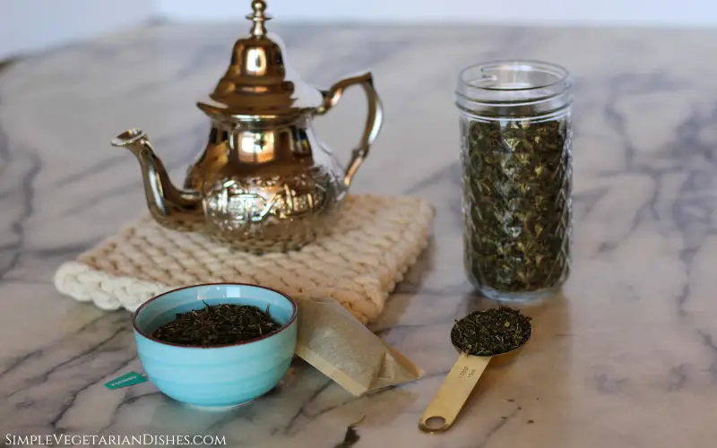 silver pot on white potholder with jar, bowl, and tablespoon in foreground